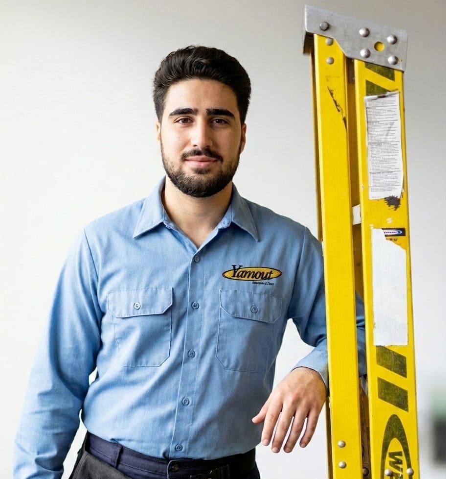 Yamout technician in a branded work shirt beside a ladder